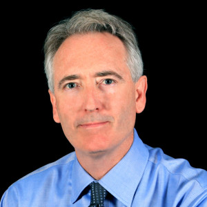 Headshot of Joe Lamond, NAMM Foundation Board of Directors, wearing a blue collared shirt and dark tie against a black background