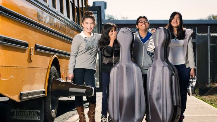 Middle School children standing by a school bus with musical instruments