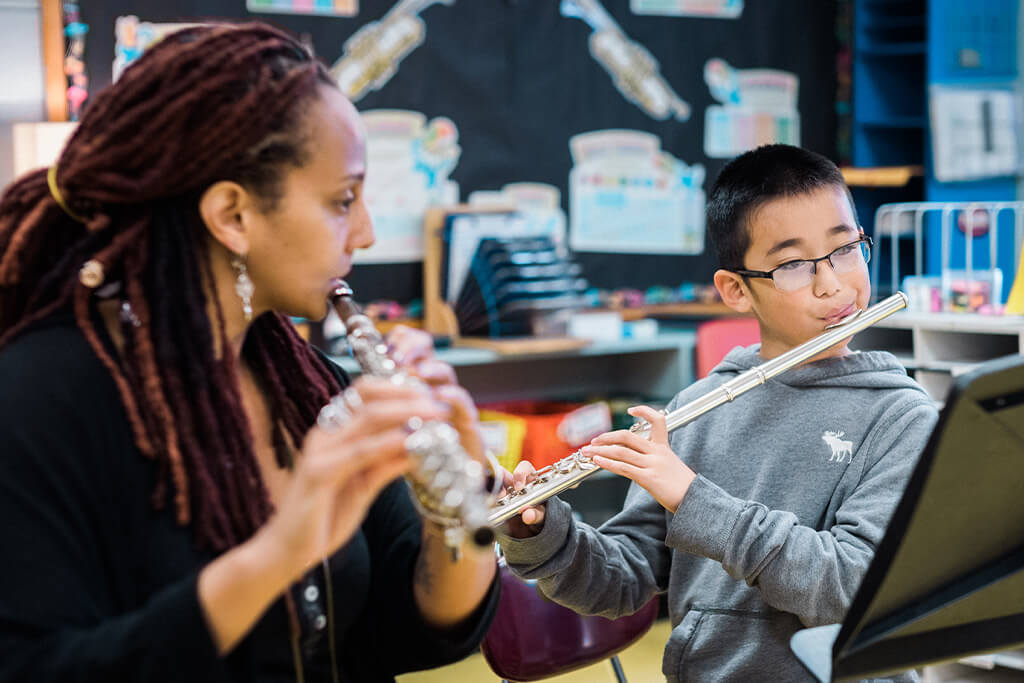 Music teacher and young student playing flutes together in a classroom.