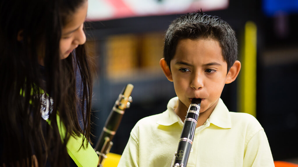 Music educator guides a student learning to play the clarinet during a classroom music lesson.