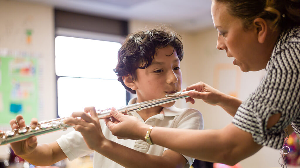 Music teacher helps a student learn to play the flute during a classroom music lesson.