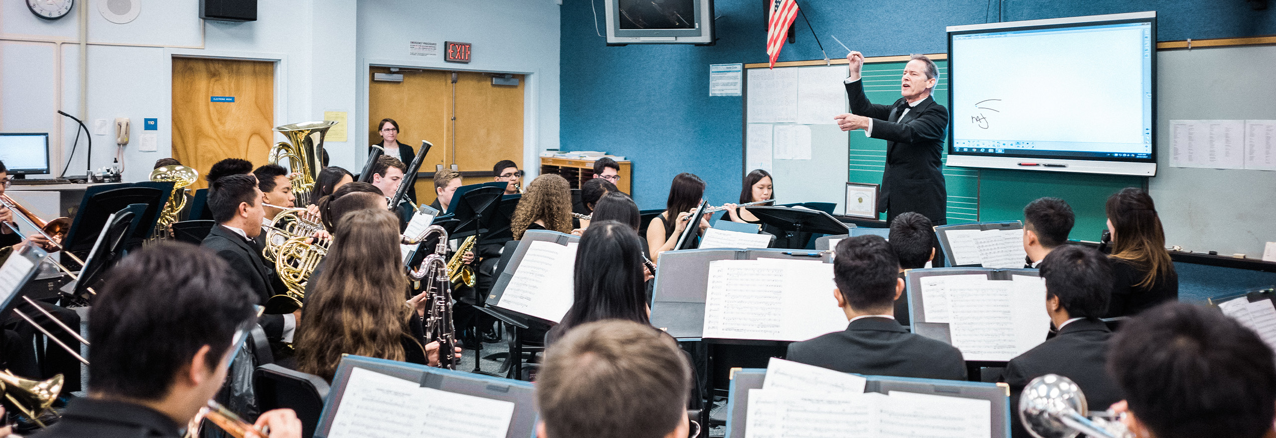 A band director conducts a full high school ensemble during rehearsal.