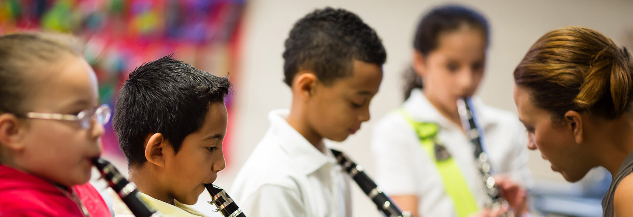 Elementary students playing clarinets in music class as their teacher guides them.