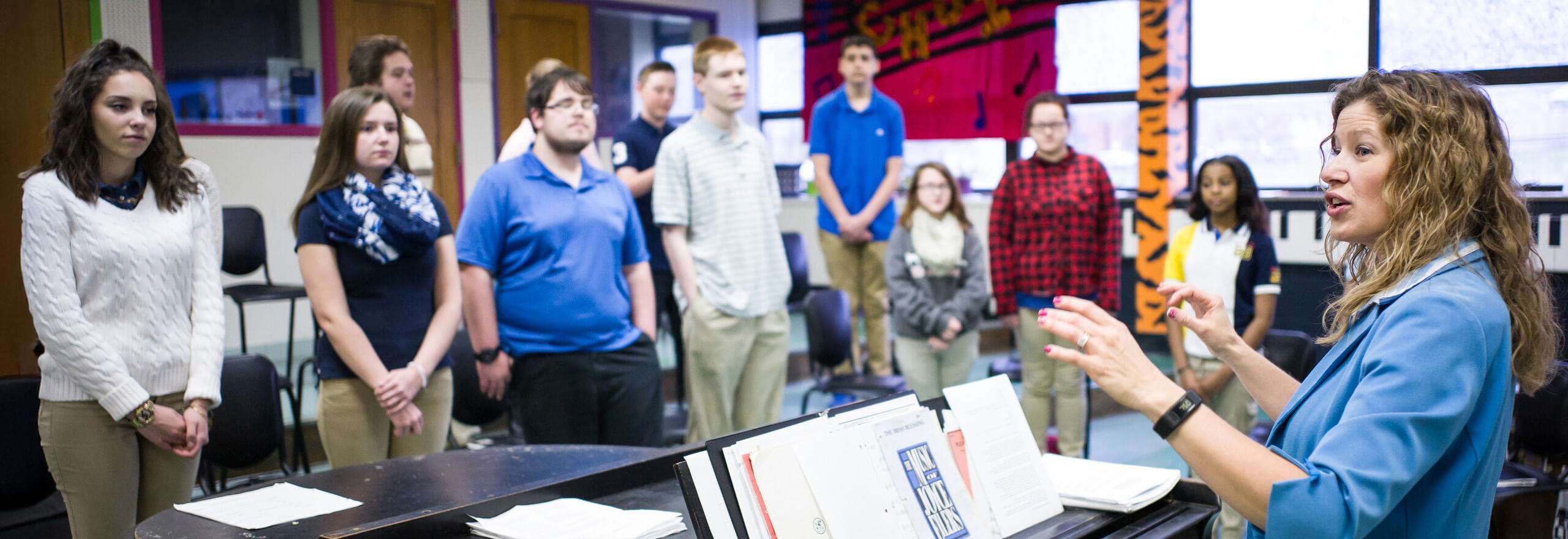 A music teacher leading a vocal rehearsal from the piano as students sing in a Choose to Teach classroom.